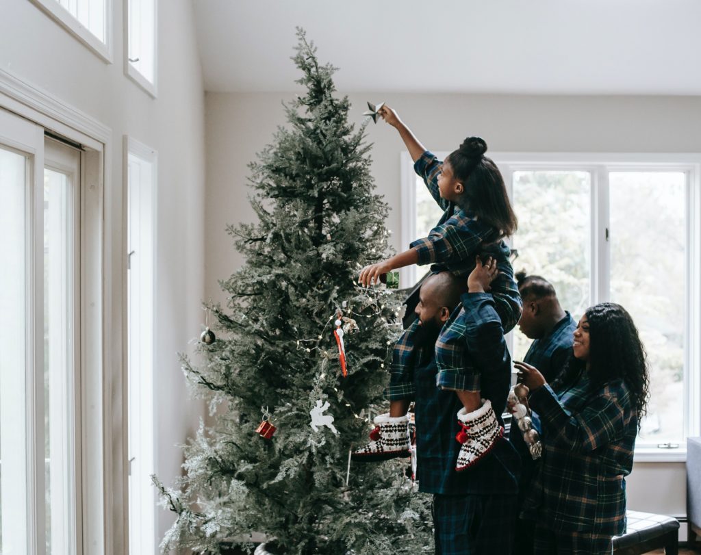 Family with matching pajamas decorating a Christmas tree together.